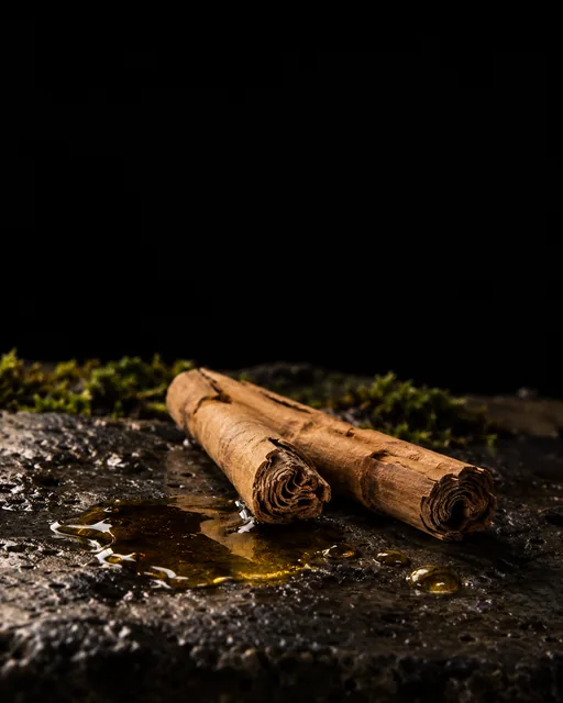 Amber cinnamon bark oil beside two Ceylon cinnamon quills on wet black basalt