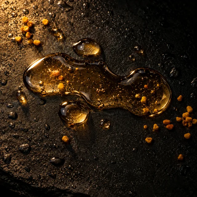 Clear golden serum drops pooling on dark wet stone among bee pollen granules